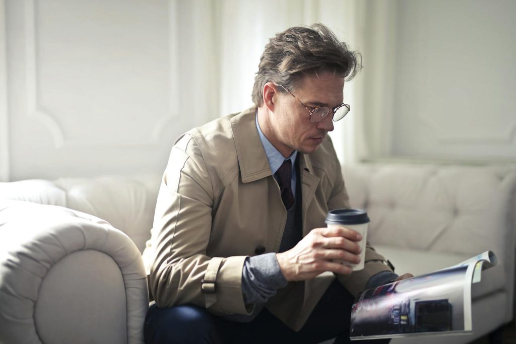 Professional man in a suit reading a magazine with a coffee cup in a modern lounge.
